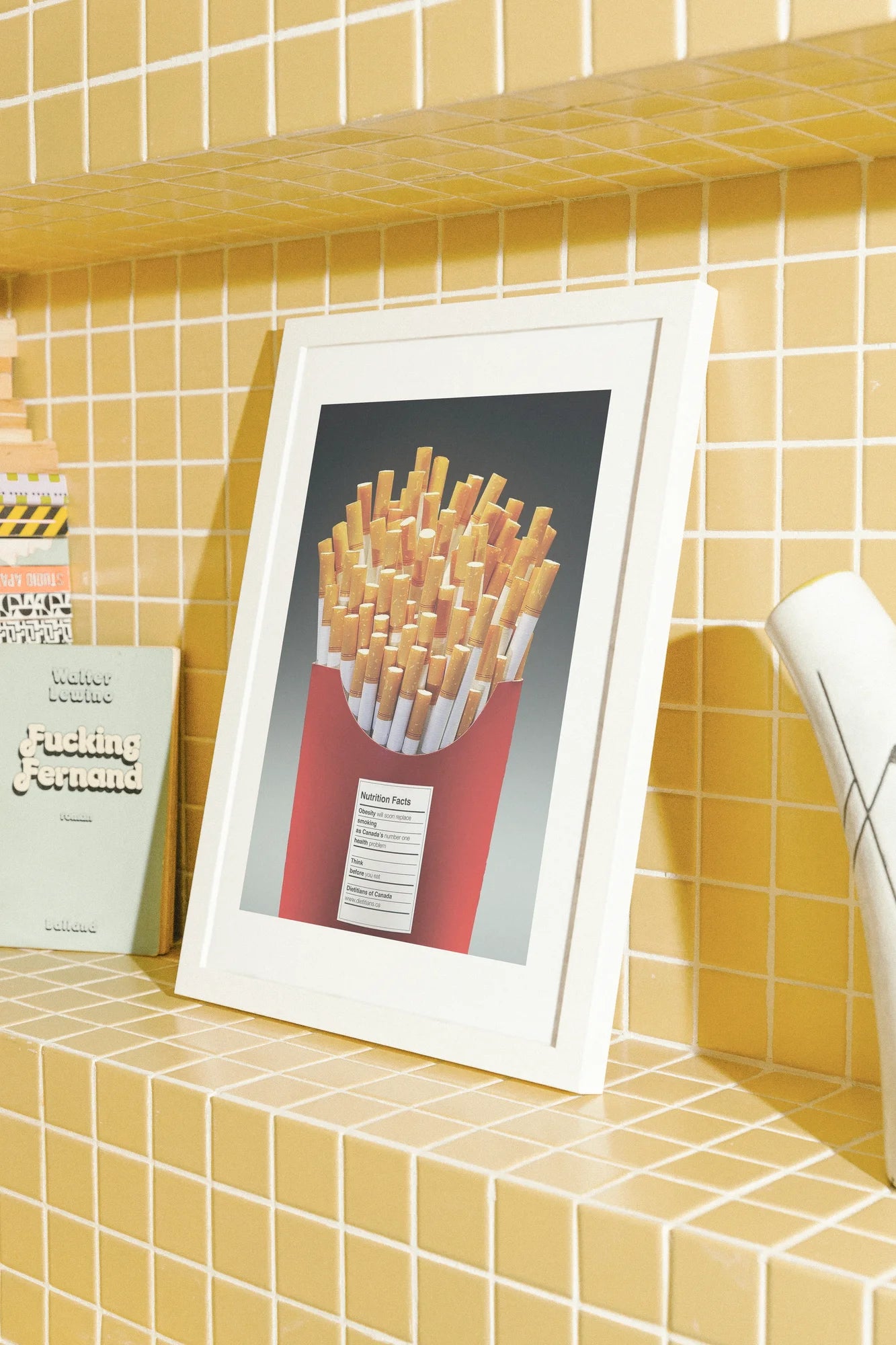 Une friteuse rouge contient une pile de cigarettes, leurs teintes orangées brillant sur une étiquette nutritionnelle d'un blanc éclatant. Cette composition résolument minimaliste capture la juxtaposition du consommateur.. minimalist, orange, red, still life, vibrant, yellow