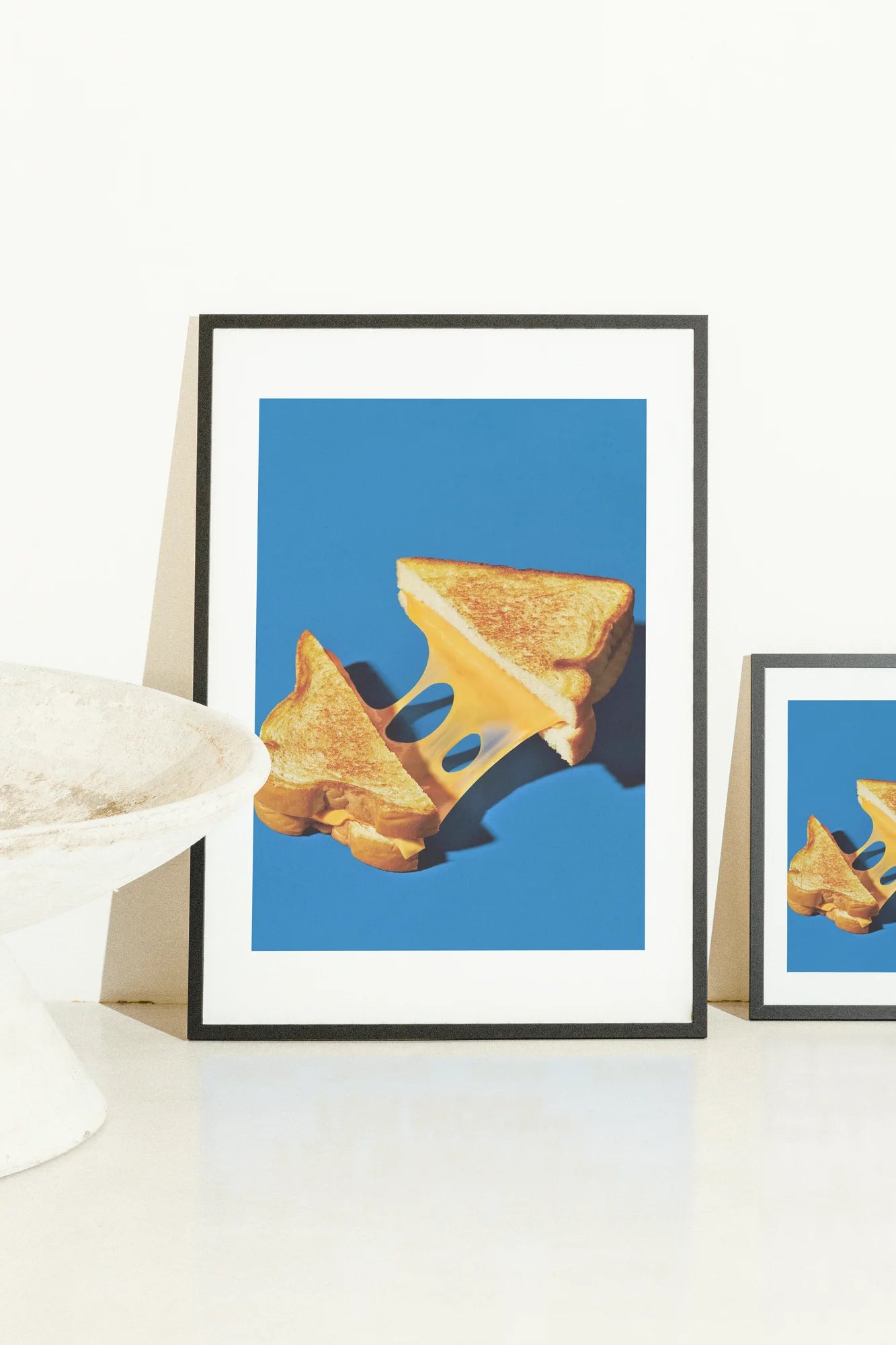 Contraste saisissant entre des pains dorés chauds et une toile bleue froide capture un grilled cheese fendu avec du fromage étiré, évoquant des textures riches et une chaleur appétissante.. blue, photographic, still life, warm, white, yellow