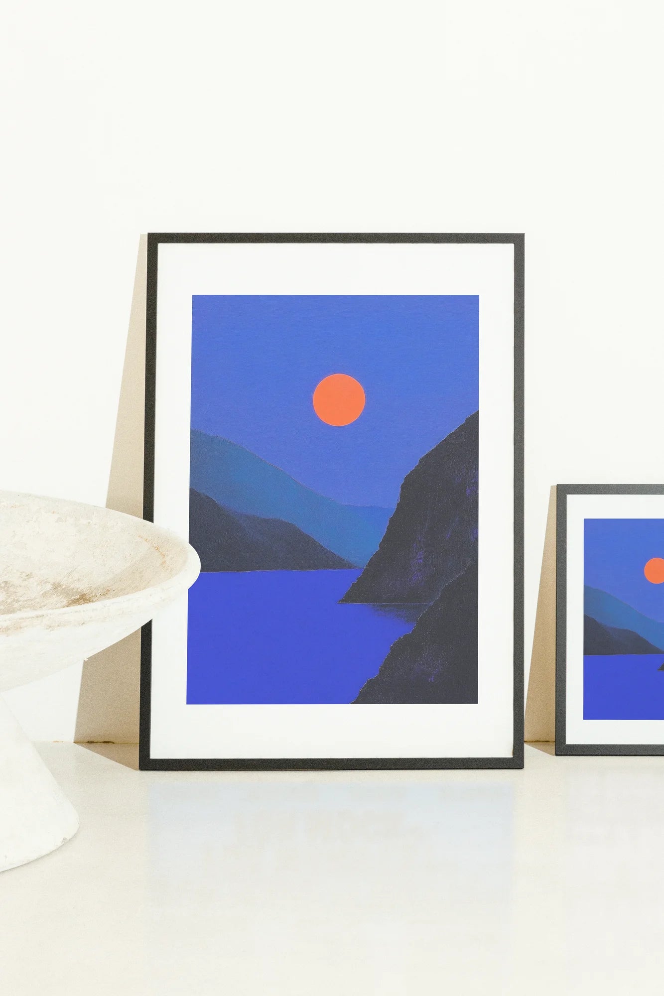 Des teintes plates audacieuses contrastent une lune orange lumineuse sur des eaux d'un bleu profond, flanquées de silhouettes sombres. Un paysage minimaliste capturant un mystère serein.. celestial, minimalist, serene