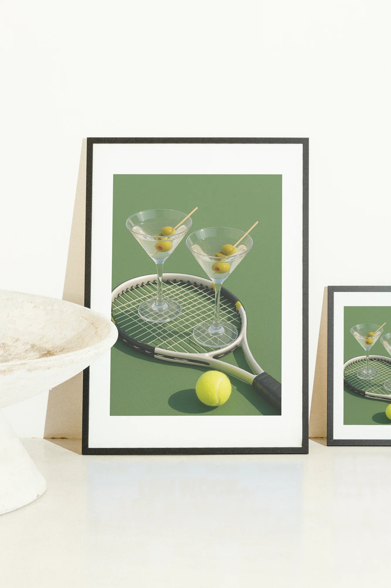 Une scène ludique et légère présentant des olives dans deux verres à martini et une raquette de tennis sur une surface verte. Avec les accents jaunes de la balle, cette œuvre d'art réaliste capture un. green, photographic, playful, vintage, yellow