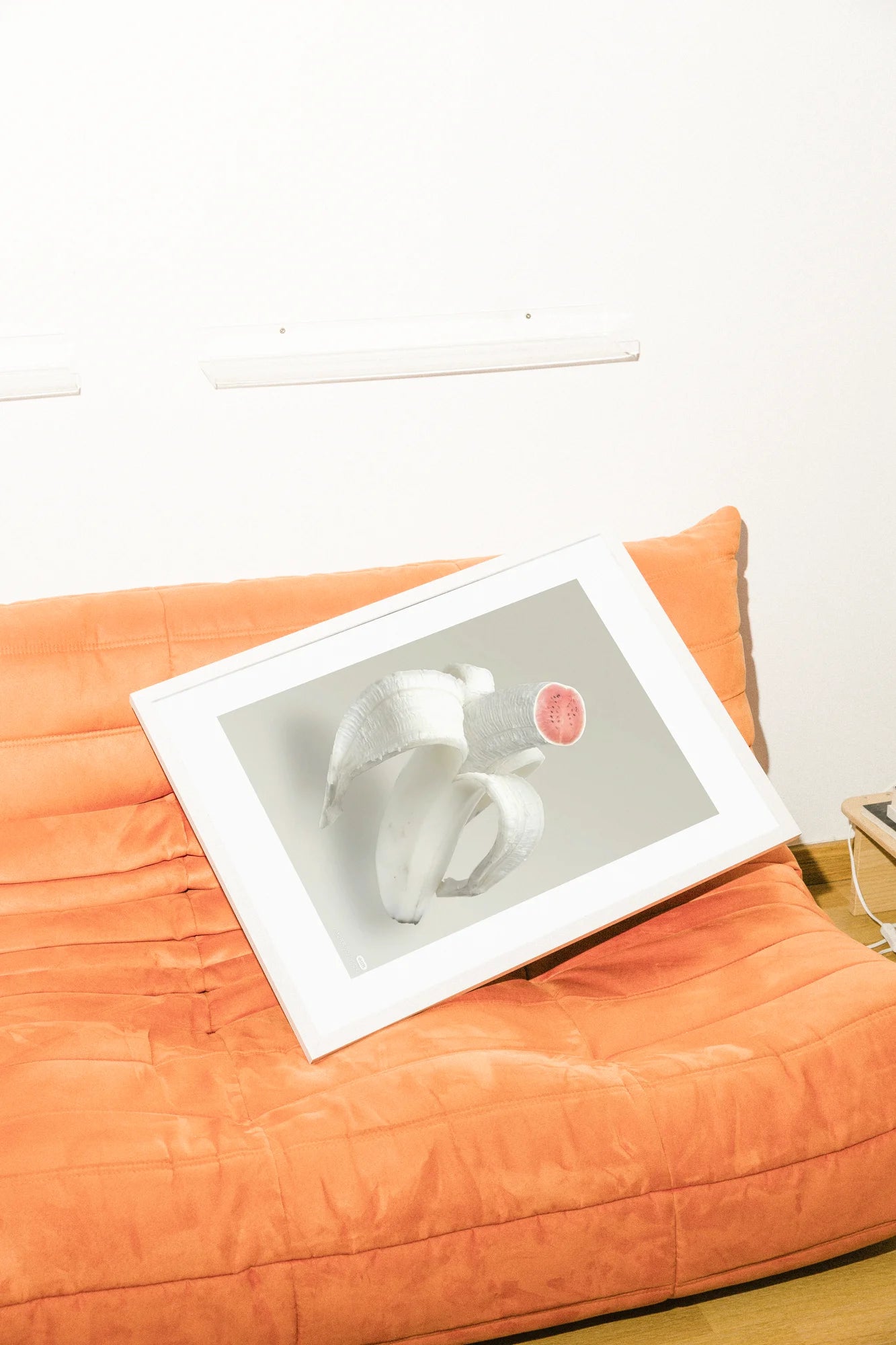 Une juxtaposition surréaliste de banane pelée et de tranche de pastèque, rendue dans des tons blancs et rouges atténués sur un fond neutre. Une composition minimaliste met en valeur la texture naturelle. minimalist, photographic, pink, red, surreal, white