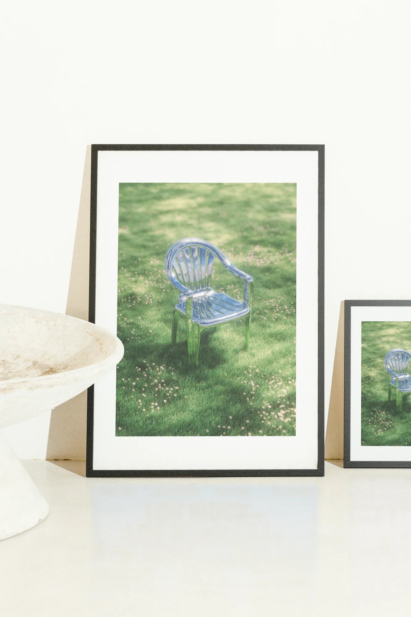 Une chaise en plastique bleue solitaire repose au milieu de l'herbe verte tachetée de soleil, entourée de délicates fleurs roses. Les tons froids contrastent avec la lumière naturelle chaude, capturant une atmosphère sereine, minimaliste. blue, green, minimalist, photographic, pink, serene